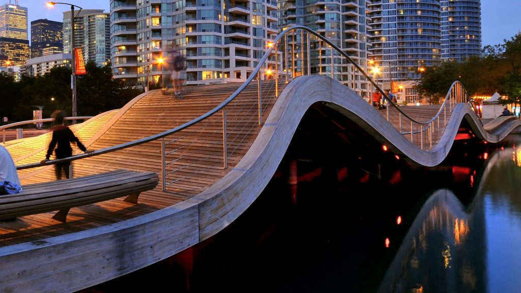 Wooden pedestrian bridge shaped like a wave, that is over a lake.